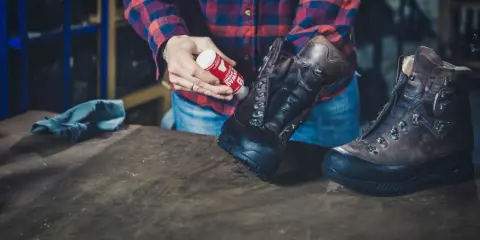Mann pflegt Hanwag Schuhe mit einem roten Pflegeprodukt. Ein blaues Tuch liegt daneben.