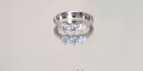 Un anello prezioso con tre diamanti scintillanti, riflesso su una superficie lucida.