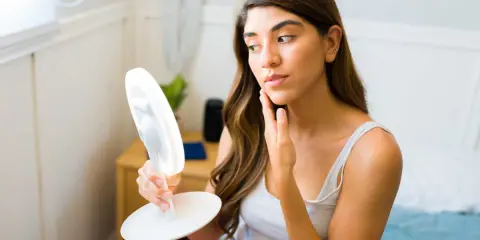 Femme examinant son visage dans un miroir lumineux, cherchant des conseils sur comment maigrir du visage.