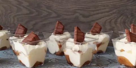 Słodkie deserki w pucharkach, przypominające tort Kinder Bueno, z kremem i kawałkami czekolady.