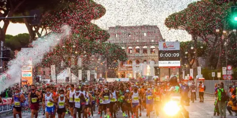 Löpare i Rom-maraton passerar Colosseum under konfettiregn.