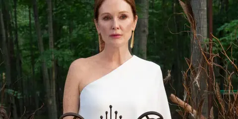 Julianne Moore i den vita klänningen i "Sirens"-serien, med en bakgrund av skog och dekorationer av fjädrar och kvistar.