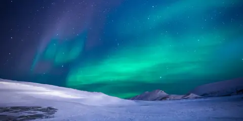 Ett magiskt blått norrsken dansar över en snötäckt fjällvärld under en stjärnklar natt.