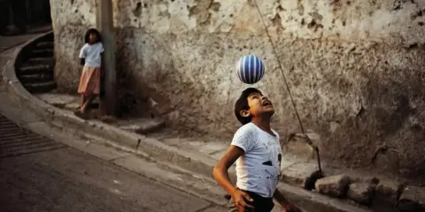 Un bambino gioca con una palla a strisce, catturato dall'obiettivo di David Alan Harvey. Una bambina osserva sullo sfondo.