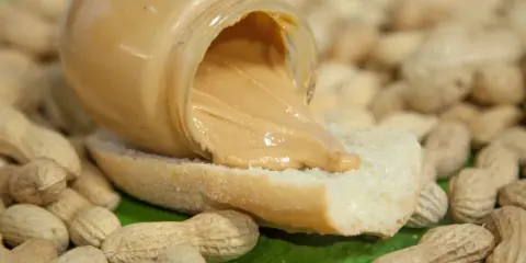 Burro di arachidi cremoso su pane, circondato da arachidi. Un piacere gustoso, ma attenzione al colesterolo!