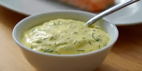 En skål med krämig romsås till lax, med dill och en sked redo att servera.