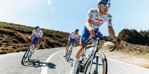 Kolarze jadący w peletonie, pokonując kolejne kilometry Tour de France. Słońce i błękitne niebo towarzyszą im w wyścigu.