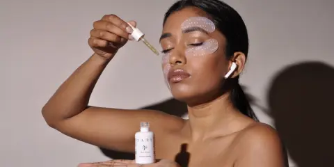 Donna applica siero con contagocce, ha maschera occhi e auricolari. Chissà ogni quanto maschera occhi per un viso radioso.