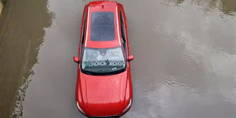 Czerwony samochód stoi w wodzie. Po powodzi czeka go osuszanie auta.
