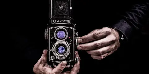 Dwie ręce trzymają aparat Rolleiflex, jedna reguluje ostrość. Sztuka fotografii, zasada złotego środka w kadrze.