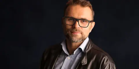 Jacek Bartosiak, autor książek, w okularach i skórzanej kurtce, patrzy w obiektyw.