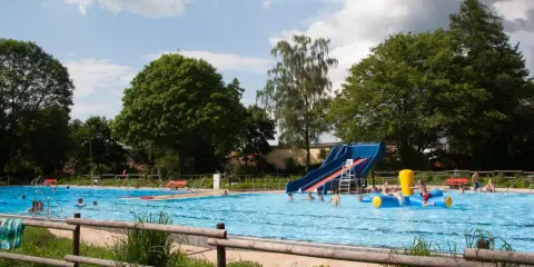 Ein sonniger Tag im Freibad Lahde. Kinder planschen im Wasser, rutschen und spielen auf einem aufblasbaren Spielzeug.