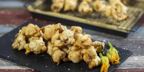 Frittelle di fiori di zucca dorate e croccanti, servite su una lavagna con fiori freschi e sale grosso.