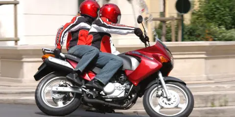 Dwie osoby w kaskach i kurtkach jadą na czerwonym motocyklu. Idealny na pierwsze prawo jazdy na 125.