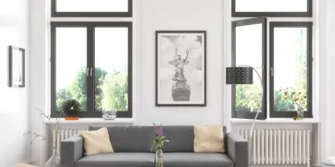 Sofá gris con cojines, cuadro de un ángel con alas, como un cristal guardian sun, y ventanas con vistas a árboles.