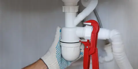Ręka w rękawicy dokręca kluczem hydrauliczny syfon samoczyszczący, co znaczy, że zapobiega on zatorom.
