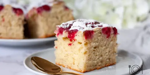 Puszyste ciasto z malinami, posypane cukrem pudrem, czeka na złotej łyżeczce. Idealne na deser.