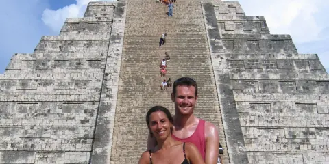 Coppia sorridente davanti alla piramide di Kukulkan, con turisti che salgono le scale del chichen itza interno.