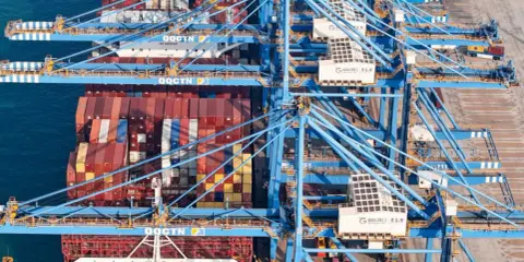 Grands portiques bleus en action, chargeant des conteneurs sur un navire. La capacité porte conteneur est impressionnante, montrant la logistique mondiale.