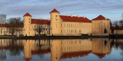 Das Schloss Rheinsberg spiegelt sich im Wasser. Die historische Altstadt von Rheinsberg zeigt sich von ihrer schönsten Seite.