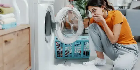 Mujer asustada por espuma saliendo de lavadora. Necesita desatascar desague lavadora para solucionar el problema.