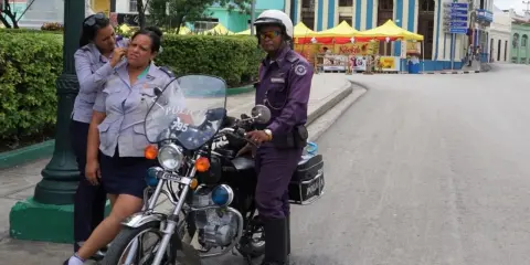 Trzy policjantki w mundurach stoją obok motocykla policyjnego na ulicy w Hawanie.