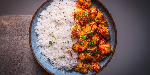 Schüssel mit weißem Reis und würzigem Bang Bang Chicken, garniert mit Koriander und Sesam.