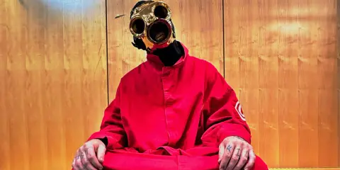 Sid Wilson i Slipknot sitter i en röd overall med en unik mask.