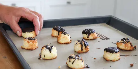 En hand lägger nyttiga kokostoppar med choklad på en plåt.