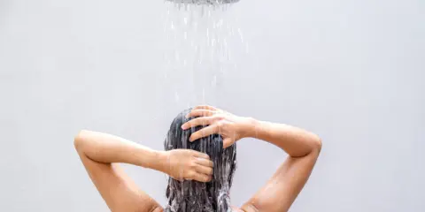 Frau wäscht sich die Haare unter der Dusche, eine natürliche Methode, um die Haare ohne Shampoo zu reinigen.