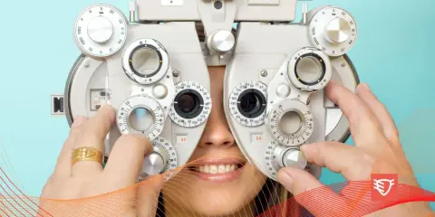 Badanie optometryczne: pacjent uśmiecha się, gdy optometrysta reguluje soczewki refraktora.