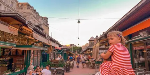 Wiedeń rynek tętni życiem. Dziewczynka na ramionach taty podziwia gwarne uliczki z restauracjami i sklepikami.