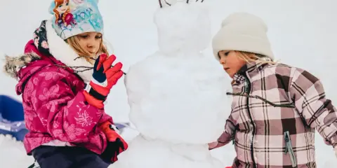 Bambini creano un pupazzo di neve in montagna, un vero natale in montagna con bambini che si divertono nella neve.