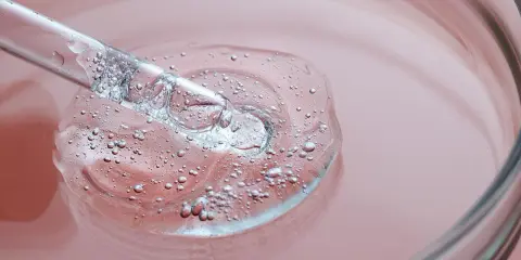 Goccia di siero trasparente con bollicine, su sfondo rosa. Un tocco di vitamina B3 per il viso.