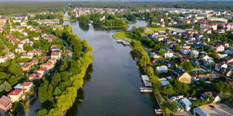 Malowniczy widok na Augustów i jego atrakcje: rzeka, zielone brzegi, domy i las w tle.