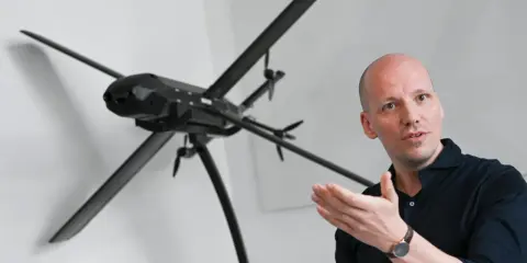 Mann erklärt ein Modell von lba drohnen, das auf einem Stativ steht.
