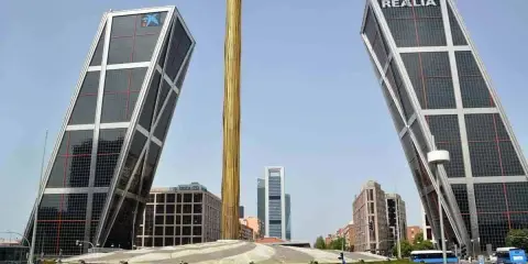 Dos icónicas estructuras diseñadas por Santiago Calatrava se alzan inclinadas, flanqueando una columna dorada.