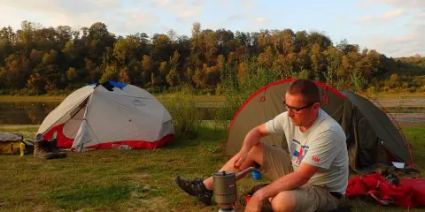 Mężczyzna gotuje przy namiotach nad jeziorem. Czas na odpoczynek po dniu pełnym wrażeń pod namioty.