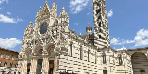 Il Duomo di Siena, con la sua imponente torre campanaria a strisce, è un must per chi cerca cosa visitare a Siena. La piazza antistante è animata da bancarelle.