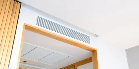 Grille de ventilation discrète pour un système de chauffage gainable, intégrée au plafond blanc et encadrée de bois.