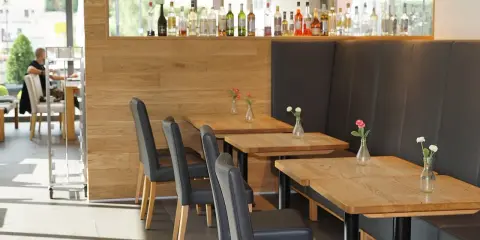 Mesas de madera con floreros y sillas negras en un restaurante. La distancia entre mesas permite un espacio cómodo.