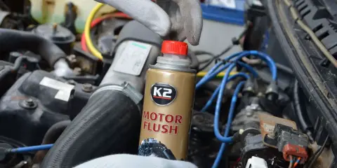 Ręka w rękawiczce trzyma puszkę K2 Motor Flush, najlepsza płukanka do silnika benzynowego, gotowa do użycia w samochodzie.