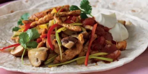 En läcker portion fajitas kyckling med paprika, champinjoner och gräddfil på en tortilla.