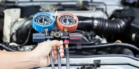 Mechanik sprawdza ciśnienie w układzie klimatyzacji, przygotowując nowy czynnik klimatyzacji do napełnienia.