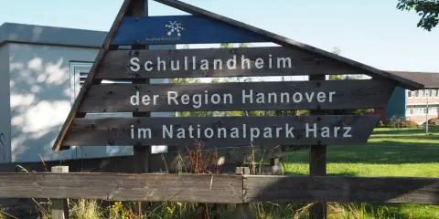 Drewniany drogowskaz "Schullandheim der Region Hannover im Nationalpark Harz" zapowiada przygodę w górach w Niemczech, być może z widokiem na szczyt Brocken.