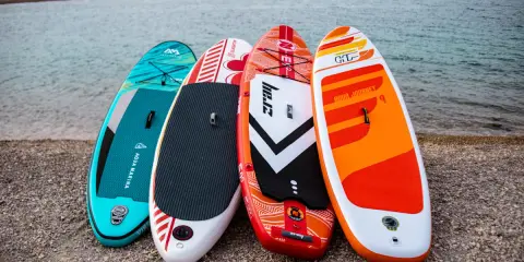 Cztery kolorowe deski SUP dla dzieci stoją na plaży, gotowe na wodne przygody.