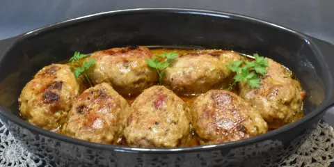 Pyszne roladki z mięsa mielonego z piekarnika, polane sosem i udekorowane natką pietruszki, prezentują się apetycznie w czarnej brytfannie.