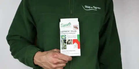 Osoba w zielonej bluzie trzyma opakowanie Lepinox Plus, biologicznego insektycydu zwalczającego gąsienice motyli. Idealny do ekologicznych upraw.