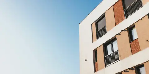 Façade d'un immeuble moderne avec balcons et volets roulants, idéal pour mettre son appartement en location. Ciel bleu clair.
