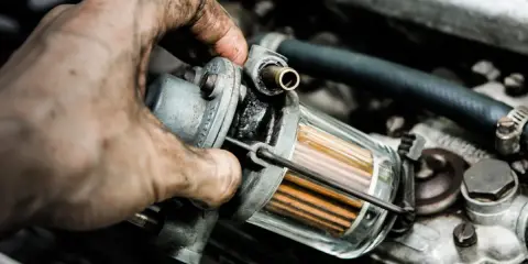 Brudna ręka mechanika wymienia zapchany filtr gazu. Objawy problemów z silnikiem mogą być różne, ale czysty filtr to podstawa.